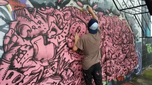Man painting a pink graffiti style on a wall in houston texas known as the houston graffiti park wall