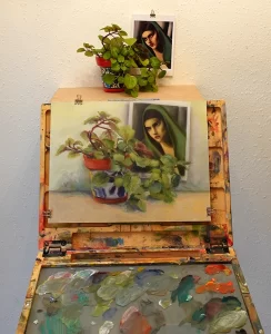 A composition of house plants and a Tamara de Lempicka postcard from the Museum of Fine Arts in Houston sits against a back wall with a painting easel in front holding an oil painting of the scene described.