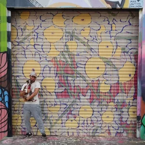 A man holding a boston terrier dog standing in front of a mural painted on a corrugated door in houston texas