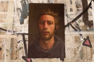 A small wood panel sits atop a surface that has lots of splattered paint marks on it. The wood panel has an oil painting portrait on it of a man in a shadowy environment. 