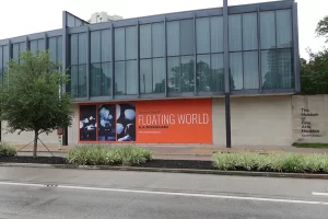 The facade of the Museum of Fine Arts with a large banner advertising the Floating World exhibit on a cloudy day in Houston, Texas.